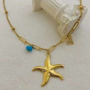 Collier étoile de mer doré avec perle bleue et lettre A sur fond blanc texturé