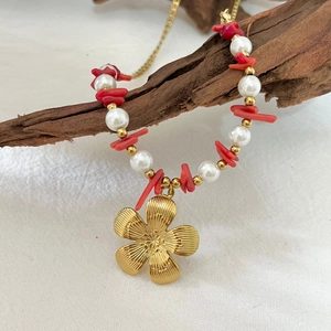 Handmade necklace with red coral chips, white pearls and gold flower pendant on wood