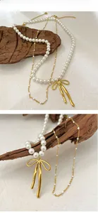 Détail du collier de perles avec pendentif nœud doré et chaîne fine superposée