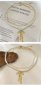 Détail d'un collier de perles à double rang avec pendentif nœud doré et chaîne fine