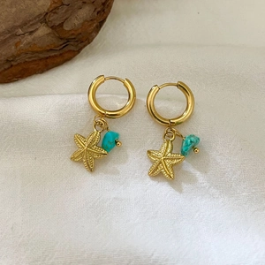 Golden starfish and turquoise stone earrings on textured white fabric background