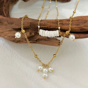 Double-layered golden stainless steel necklace with baroque pearls on a rustic wood branch
