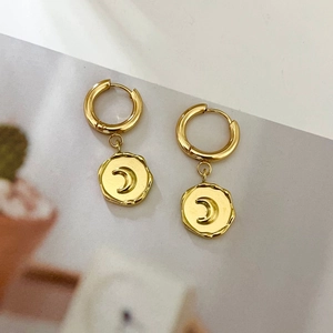 Minimalist 18K gold moon pendant hoop earrings on artistic magazine background