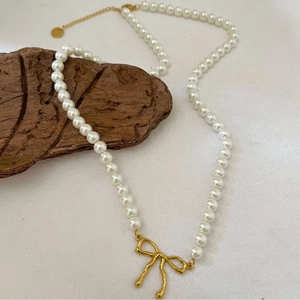 Collier de perles fait main avec pendentif nœud plaqué or 18k sur fond de bois naturel