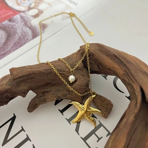 Double-layered gold starfish necklace with elegant pearl pendant on rustic wood branch