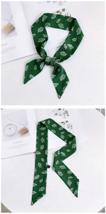 Détail d'un foulard étroit vert foncé avec imprimé feuilles blanches noué en boucle