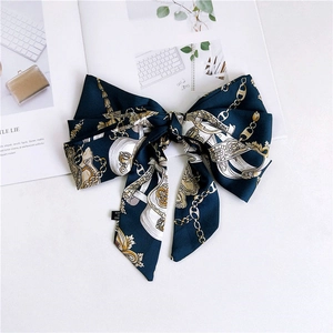 Detailed flat lay of a blue satin scarf with vintage gold chain prints and ribbon knot