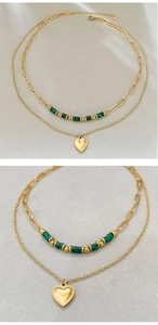 Détail d'un collier doré double épaisseur avec pendentif cœur et perles vertes