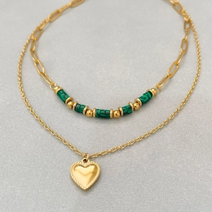 Collier double épaisseur en or avec perles vertes et pendentif cœur sur fond gris