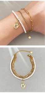 Macro detail of multi-layered gold bracelet with white pearls and Hamsa hand charm