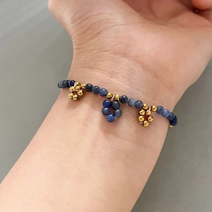 Handgefertigtes Armband mit blauen Sodalith-Steinen und goldenen Blumenanhängern am Handgelenk