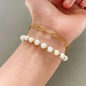 Bohemian double-layered gold paperclip and pearl bracelet set worn on a female wrist