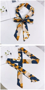 Détail du foulard twilly en soie à motif géométrique noué en nœud et posé à plat sur table