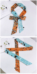 Détail d'un foulard de 155 cm bleu et orange noué en ruban avec des motifs de grues