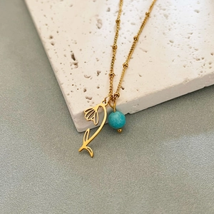 Gold tulip flower necklace with turquoise bead pendant on textured stone background