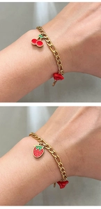 Detailed view of gold Figaro chain bracelet featuring red cherry and strawberry pendants