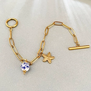 Bracelet étoile de mer doré avec perle céramique et chaîne trombone sur fond gris