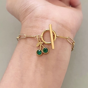 Détail d'un bracelet en chaîne trombone doré avec pendentif cerise en strass verts