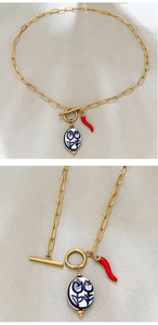 Detail of gold chain necklace featuring a red chili pendant and blue ceramic charm with OT buckle