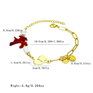 Gold chain bracelet with red coral charm, white bead and foot pendant on white background
