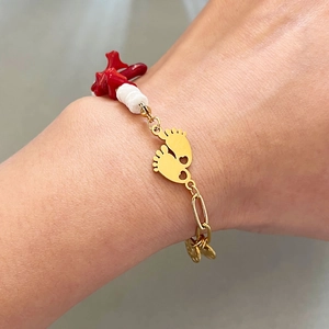 Gold chain bracelet with baby feet charms, red coral accents and white beads on wrist