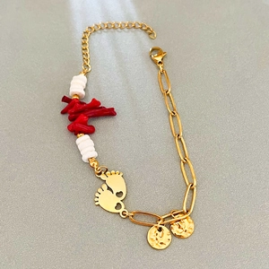Gold chain bracelet featuring red coral accents, white beads, and foot shaped charms