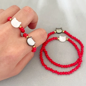 Red beaded cat charm rings and bracelets set with golden accents on a model hand