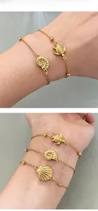 Detailed view of gold ocean charms featuring sea turtles and conch shells on wrist