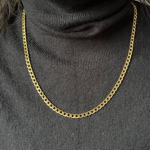 Close-up of a classic gold plated Cuban link chain necklace on a black turtleneck