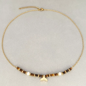 Collier vintage doré avec perles œil de tigre et pendentif queue de poisson sur fond gris