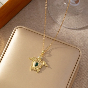 Détail collier tortue dorée avec pierre verte poire et incrustation de zircons brillants
