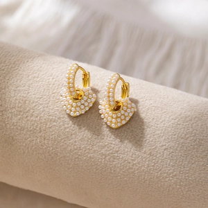 Elegant gold heart earrings with white seed pearls on a professional jewelry display stand