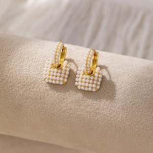 Elegant gold-plated square drop earrings with micro-set pearls on a beige display stand