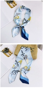 Close-up of floral print light blue silk twilly scarf tied on a stylish straw summer bag