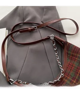 Close-up of brown leather shoulder strap and silver metal buckle on plaid bag