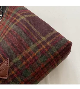 Close-up of classic wool plaid fabric and leather brand patch on shoulder handbag