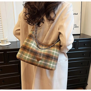 Detail of checkered woolen underarm bag with metal chain strap worn by a model