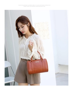 Détail d'un sac Boston tressé marron avec poignée ronde et logo doré sur fond minimaliste