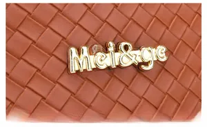 Gros plan sur la texture en cuir tressé marron avec plaque logo métallique Mei&ge dorée