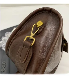 Detail view of vintage gold D-ring and hook hardware on brown leather saddle bag