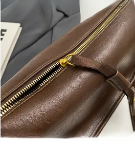 Detailed close-up of smooth gold metal zipper on textured dark brown leather saddle bag