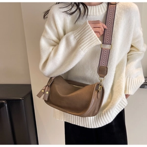 Detail of dark brown leather saddle bag with geometric jacquard strap and gold hardware