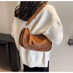Detail der karamellbraunen Satteltasche mit Ledertextur und Metallreißverschluss für Damen