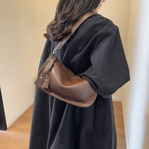 Schicke dunkelbraune Satteltasche aus Kunstleder, getragen von einem Modell im Trenchcoat