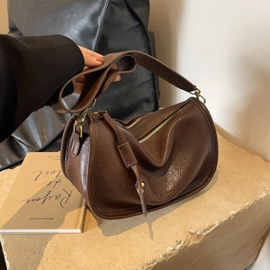 Dunkelbraune Satteltasche aus Kunstleder mit breitem Gurt auf Steinsockel