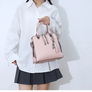 Détail d'un sac à main rose tressé avec pompon décoratif et pendentif chat métallique