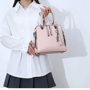 Détail d'un sac à main rose tressé avec breloque chat et pompon sur tenue élégante