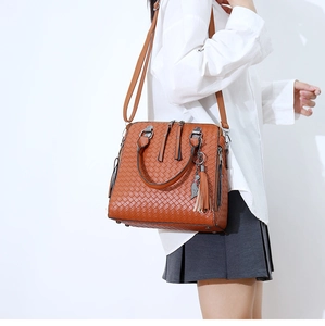 Détail du sac bandoulière tissé marron avec pendentif chat et pompon sur modèle
