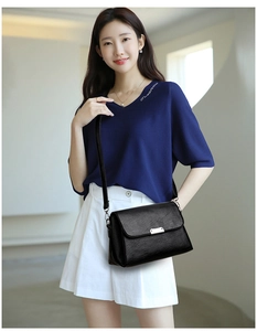 Détail d'un sac à bandoulière noir avec texture litchi et boucle argentée sur modèle