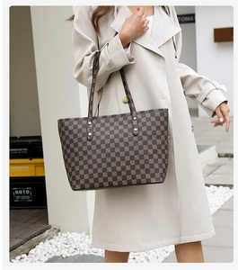 Detailed view of checkered tote bag with gold rivets and leather handles in outdoor setting